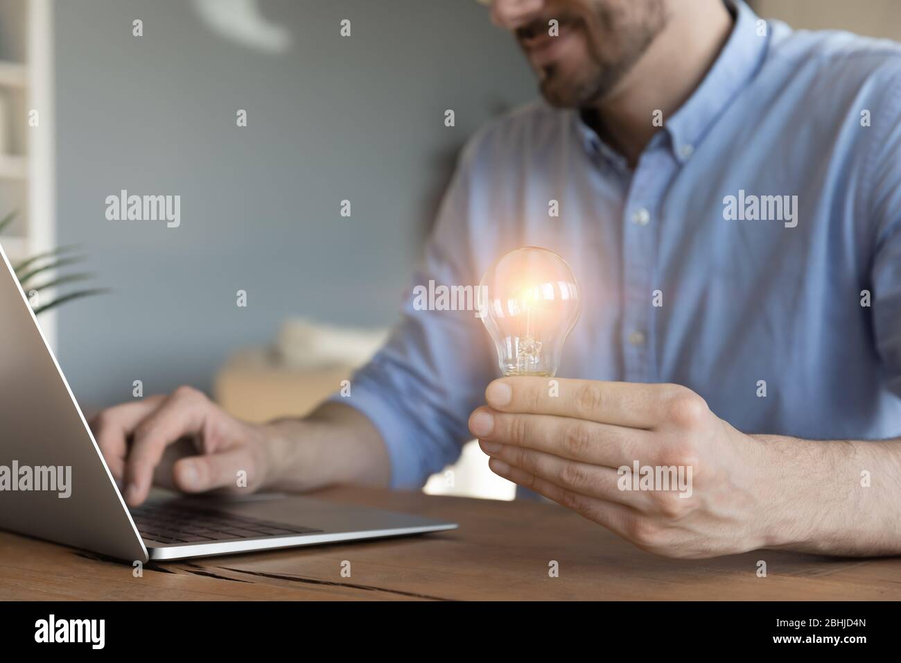 Close up businessman holding light bulb, sitting at work desk Stock Photo