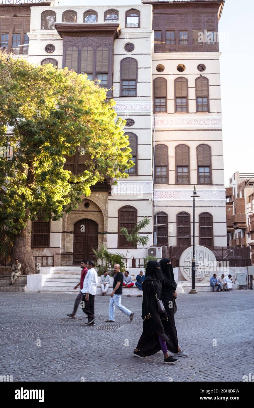 Jeddah / Saudi Arabia - January 16, 2020: Muslim women wearing abaya walking in front of wooden building in historic Al-Balad old town Stock Photo