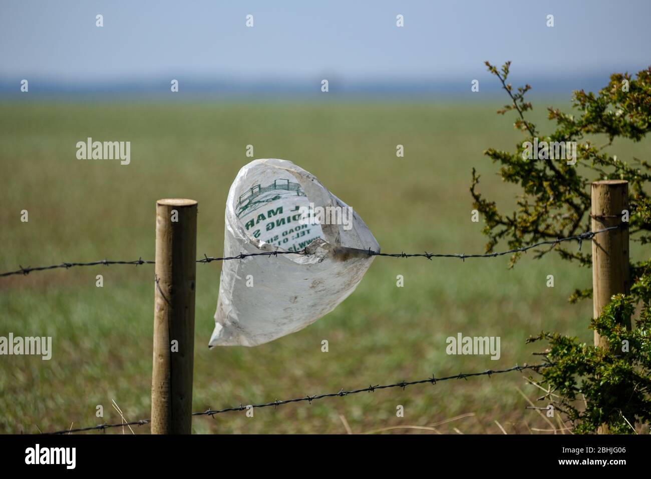 Plastic bag caught on a wire fence polluting the countryside and planet. Stock Photo