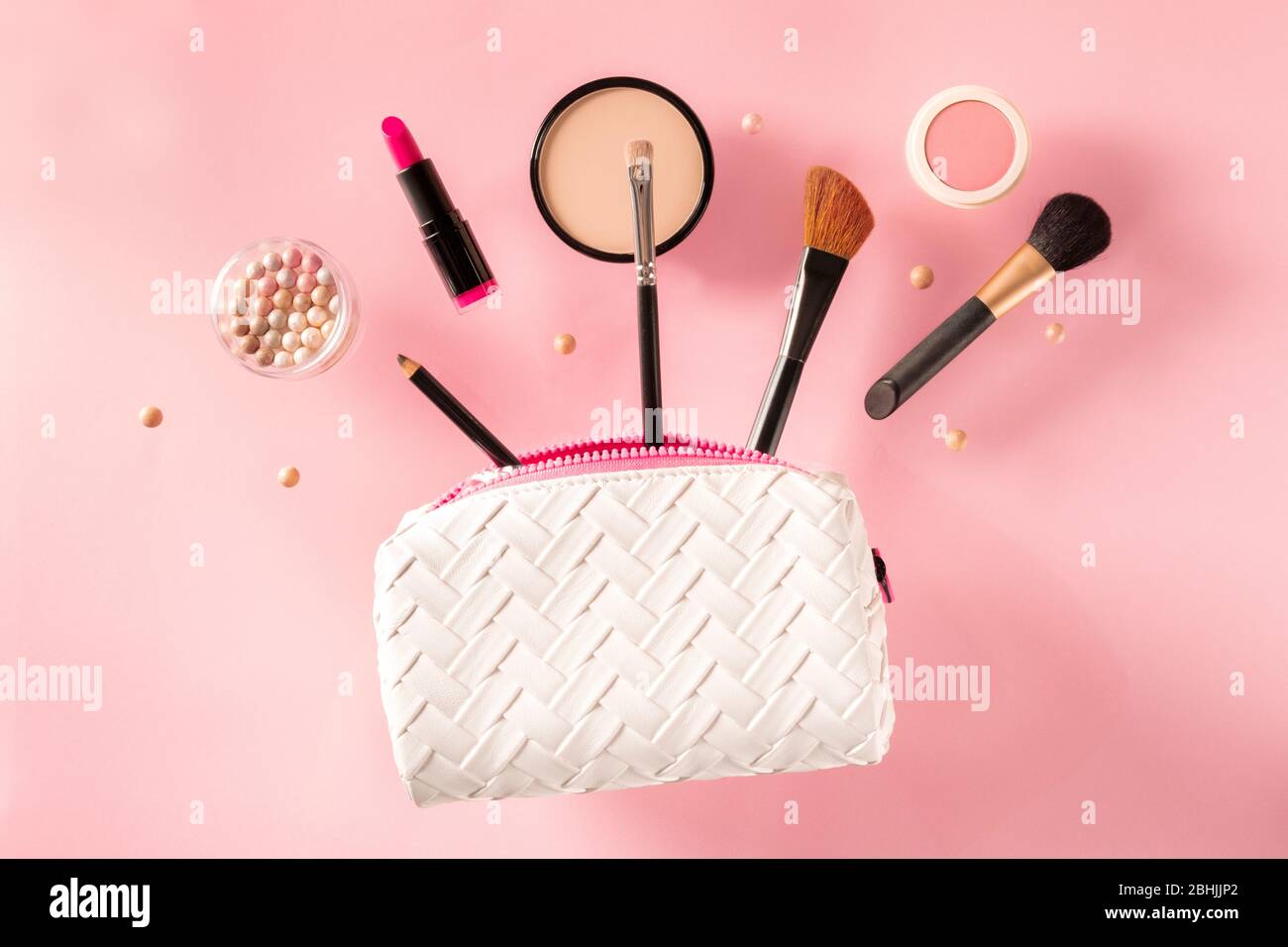 Professional makeup, flying out of a bag, on a pink background. Lipstick, brushes, powder
