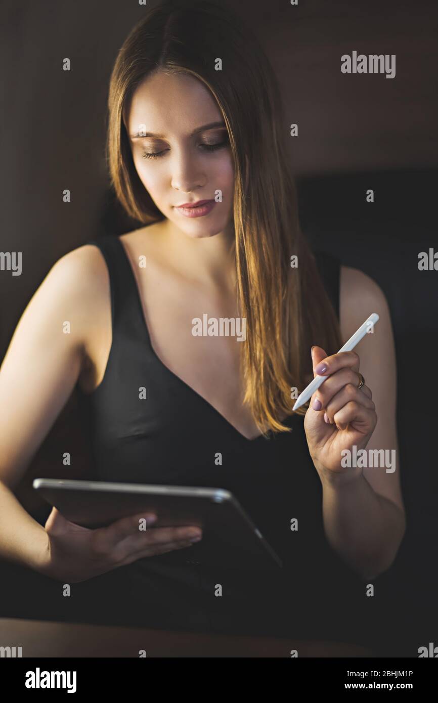 Beautiful sexy young woman wearing black dress in private jet. Female artist graphic designer drawing on digital tablet during the flight. Technology, Stock Photo