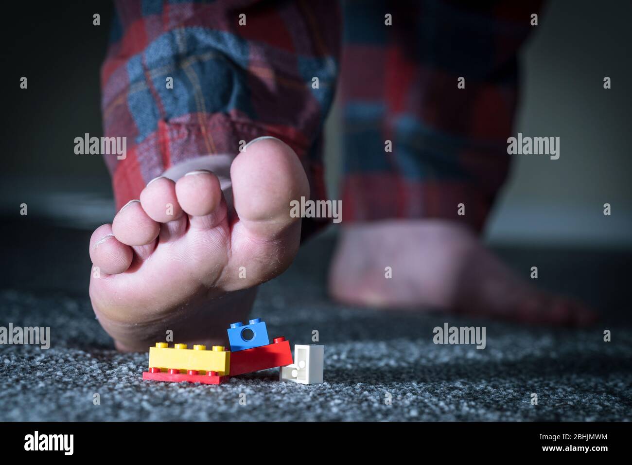 Man in his pajamas steping on Lego which was left on the floor overnight. Stock Photo