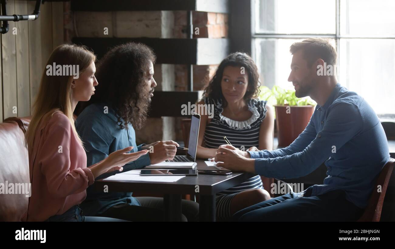Multiracial colleagues cooperate in coffeehouse working on laptop Stock Photo