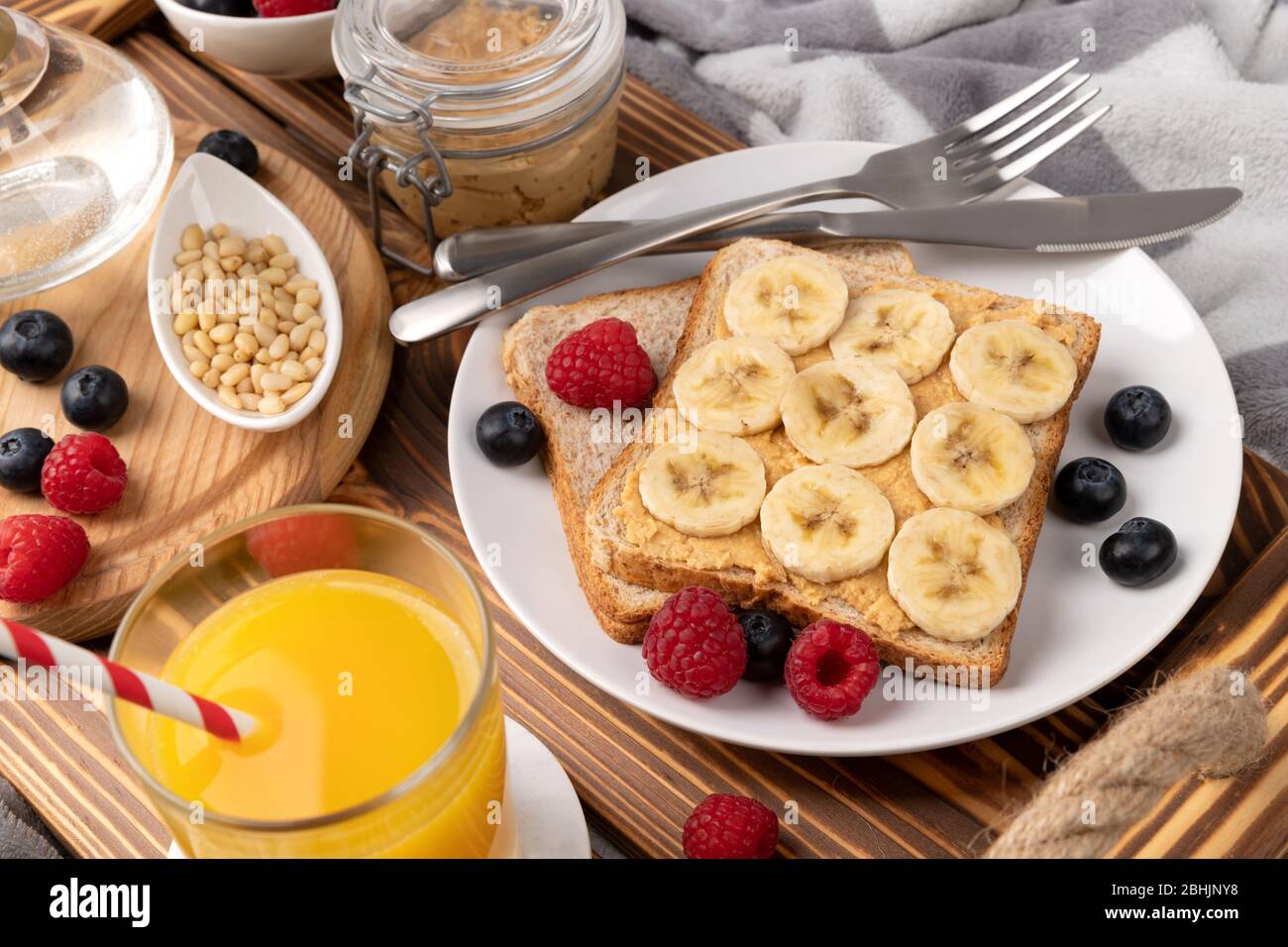 Breakfast in bed. Wooden tray with glass of orange juice and sandwich with berries Stock Photo