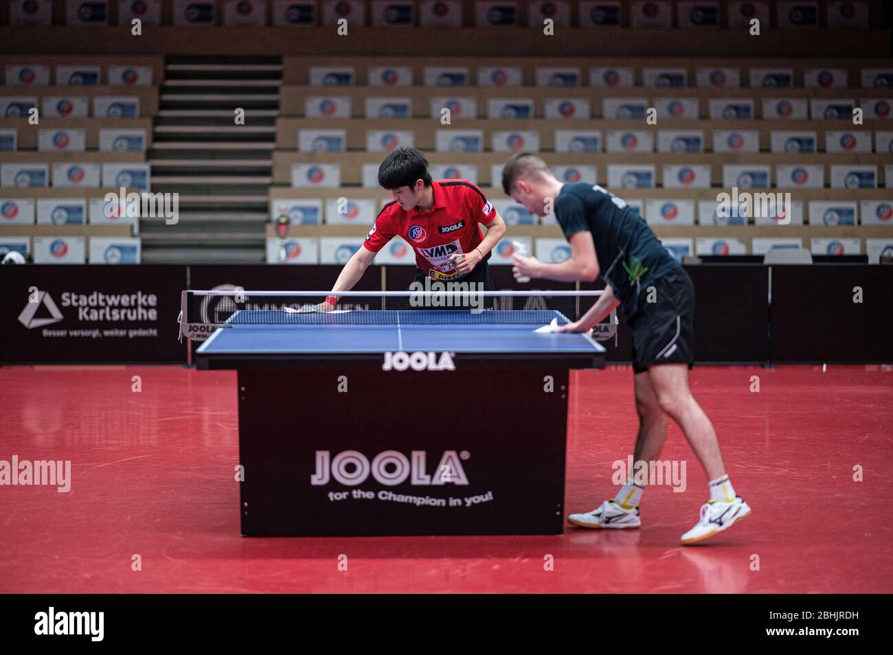 Deni Kozul (front/ASV Gruenwettersbach) rubs the table tennis table with  disinfection switch. Back: Dang Qiu (ASV Gruenwettersbach). In the  background there are cardboard stands on the empty stand instead of the  spectators.