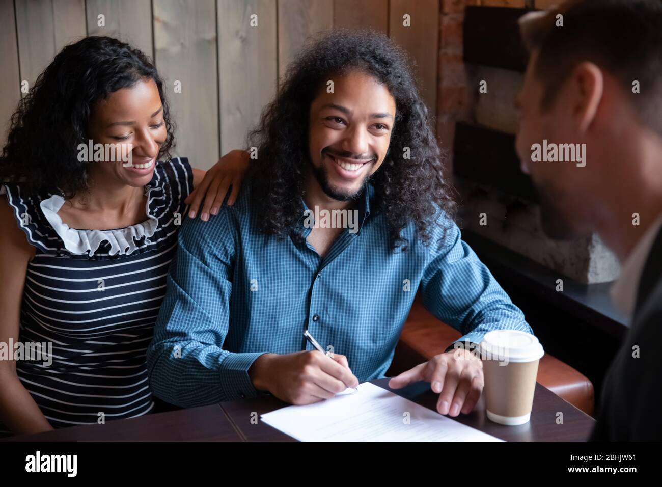 Happy multiracial couple sign document closing deal in cafe Stock Photo
