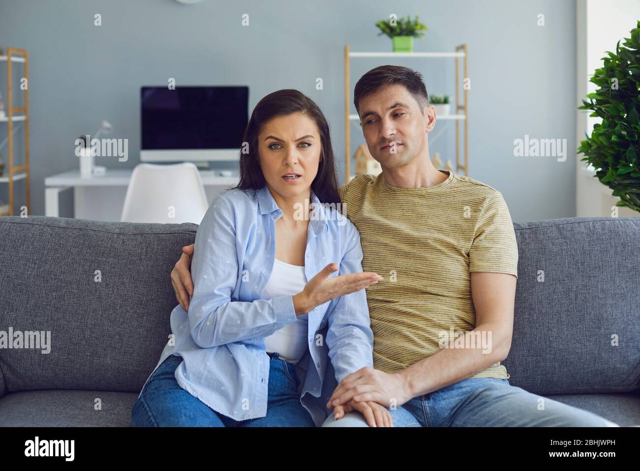 A couple in a serious emotional mood with problems looks at the camera while sitting on the couch. Stock Photo