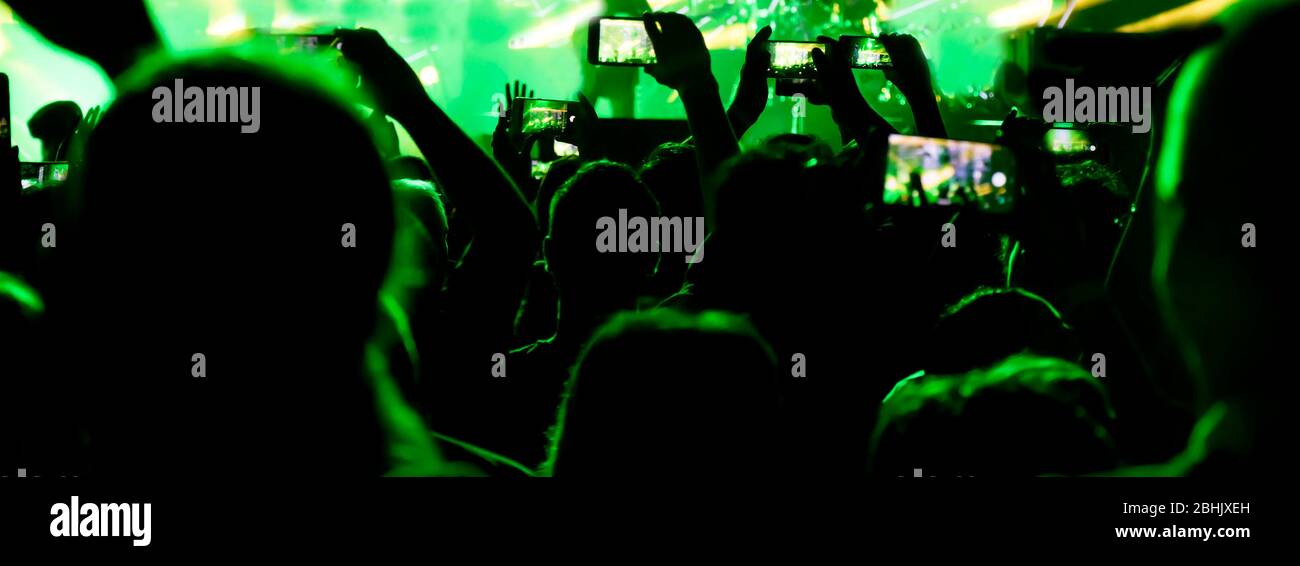 Collecting digital memory is loosing capability of being present, silhouettes of crowd of people shooting the concert with  mobile phones, in green li Stock Photo
