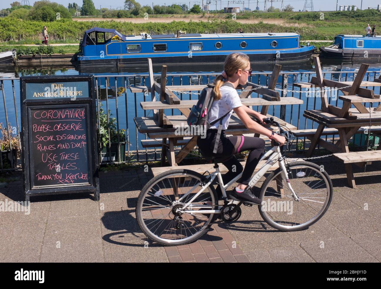 Cyclist in London rides past closed pub by River Lea during coronavirus lockdown with sign asking public to respect social distancing during Covid-19 Stock Photo