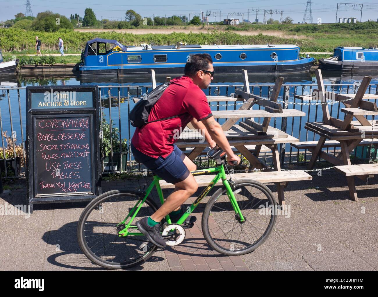 Cyclist in London rides past closed pub by River Lea during coronavirus lockdown with sign asking public to respect social distancing during Covid-19 Stock Photo