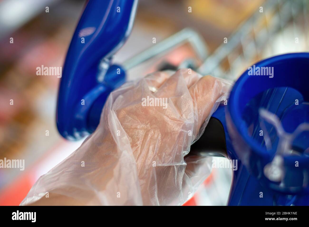 Closeup hand with disposable plastic glove pushing a shopping cart for safety measures during covid-19 coronavirus pandemic Stock Photo