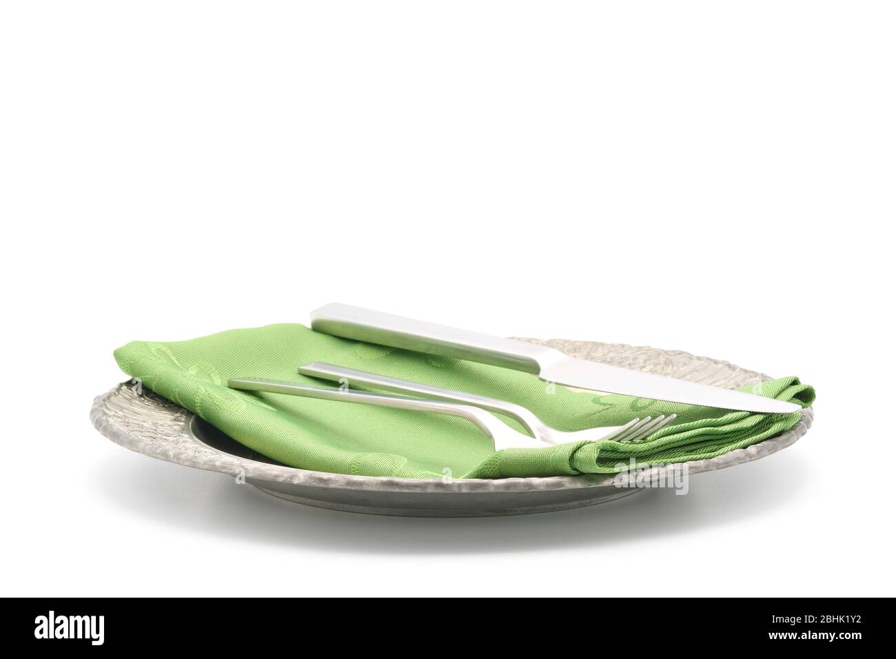 Ornate metal plate and a brushed silver flatware set photographed on a white background with ample copy space. Stock Photo