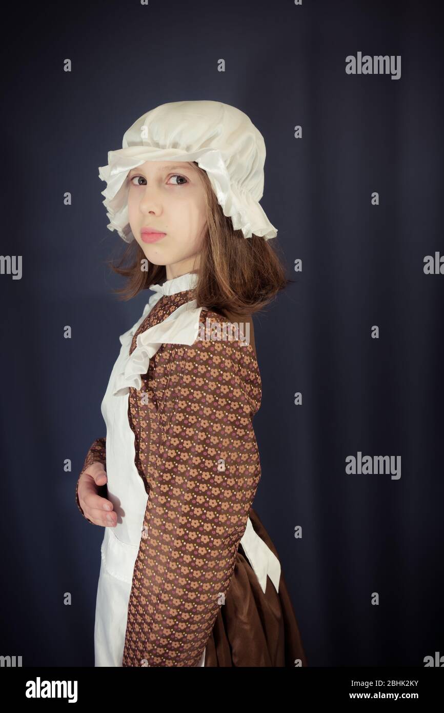 A girl dressed as a Victorian schoolgirl or maid in white mob cap and apron - standing tall and looking at camera Stock Photo