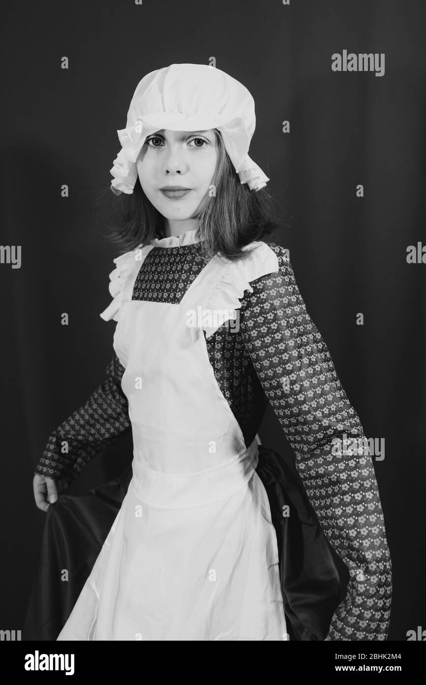 Black and white vintage style photo of girl dressed in a Victorian maid costume with mop cap for World Book Day Stock Photo