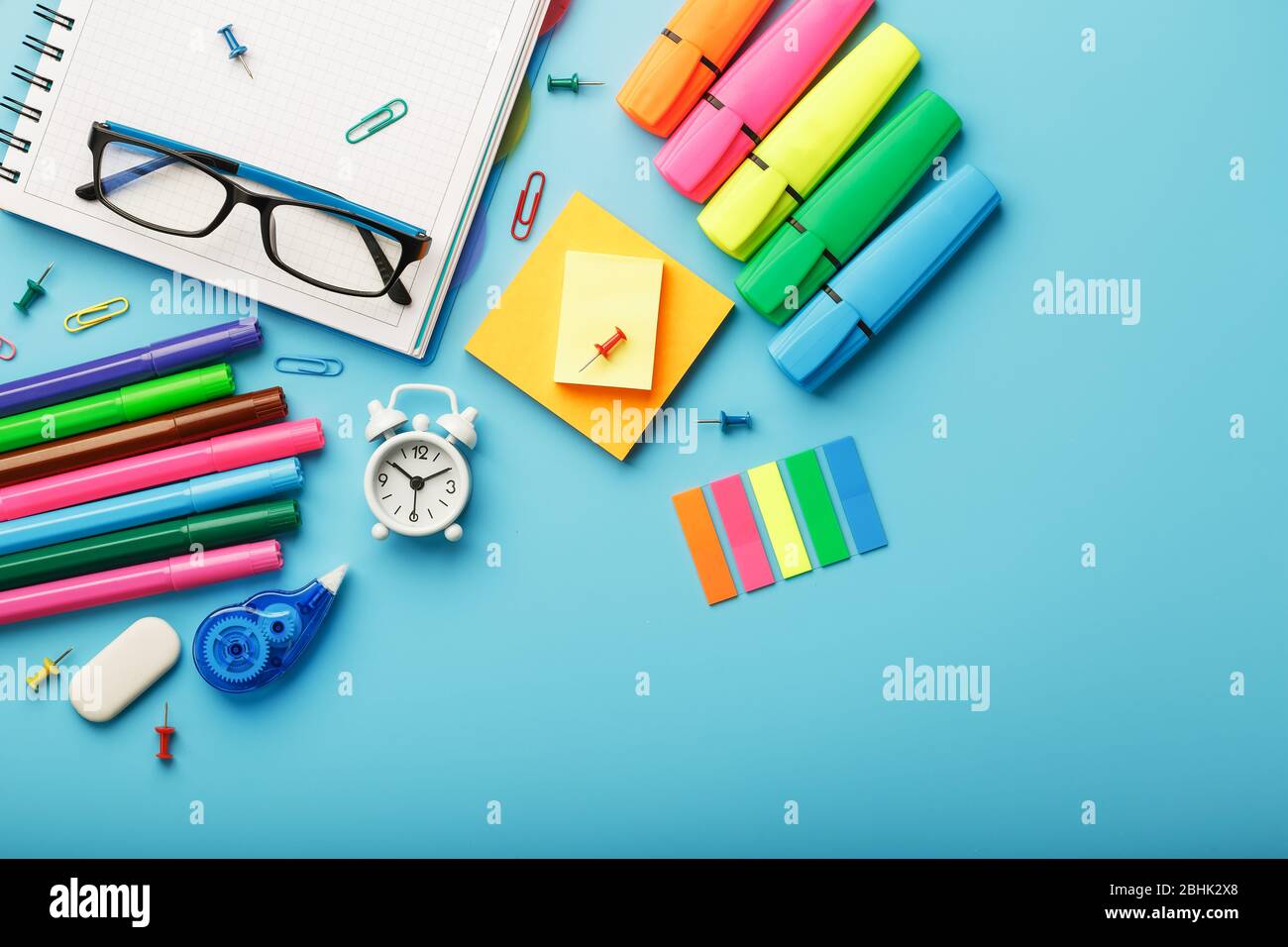 Colorful Stationery items with an alarm clock lie on a blue background ...
