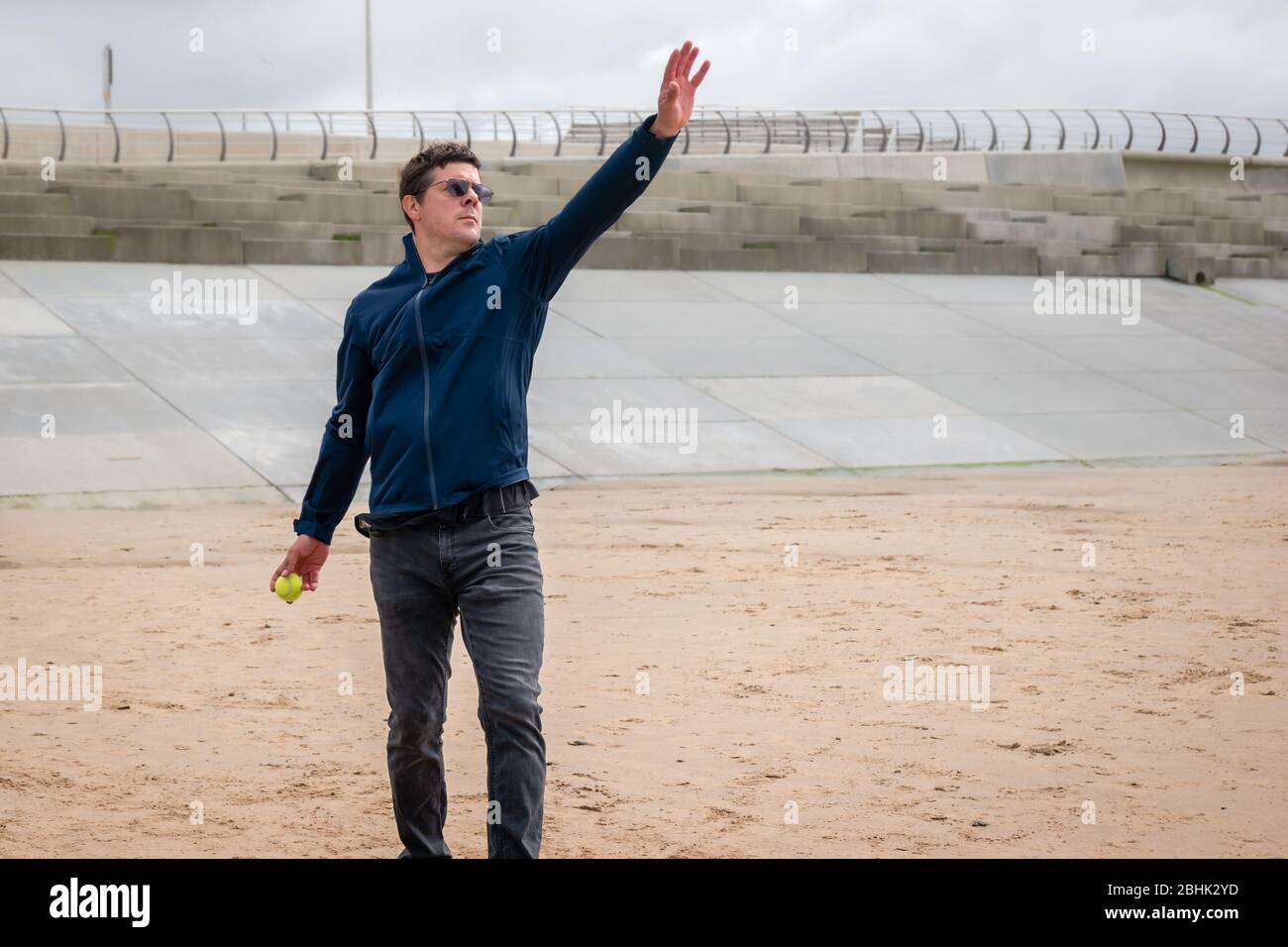 A man in a jacket playing cricket with a tennis ball on the beach Stock Photo