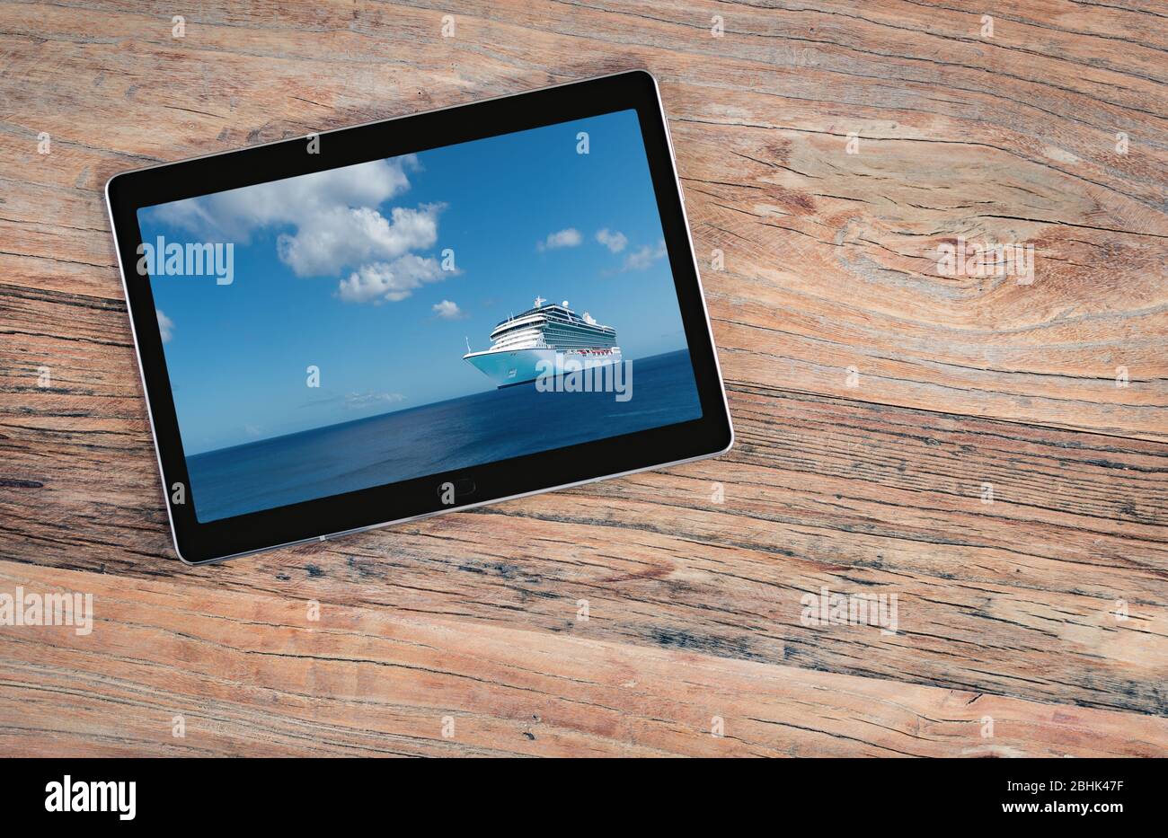 Cruise ship on screen of digital tablet. Top view of mobile pc device on old wooden table. Cruise travel and travel agency sales concept. Stock Photo