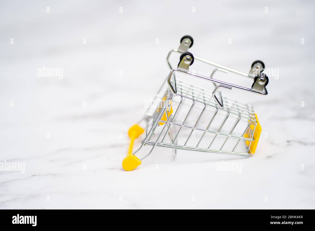Empty inverted shopping cart on white marble background. Stainless steel shopping trolley upside down. Business, mall, market, shopping concept. Stock Photo