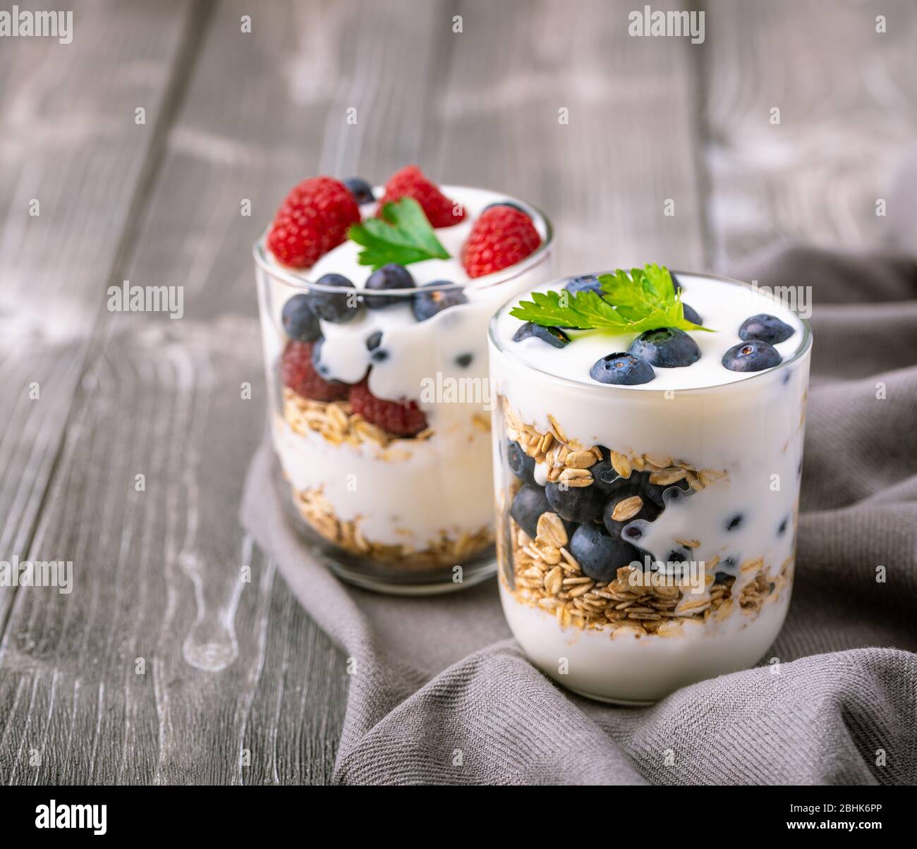 White yogurt in glass jar with fruits on grey background. Stock Photo
