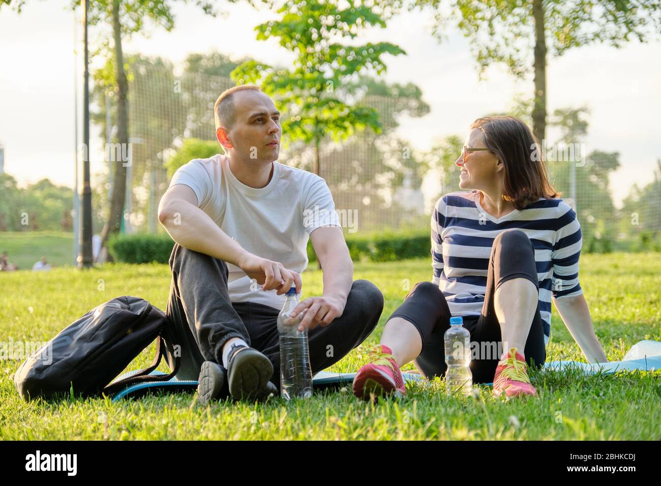 Middle-aged couple sitting on yoga mat, man and woman talking relaxing drinking water. Active healthy lifestyle, relationship, sport, fitness in matur Stock Photo