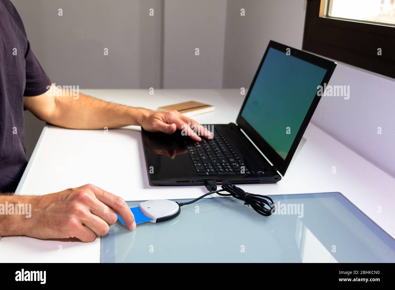 A man prepares to work from home with his laptop by identifying himself through a card reader. Covid-19 confinement concept Stock Photo