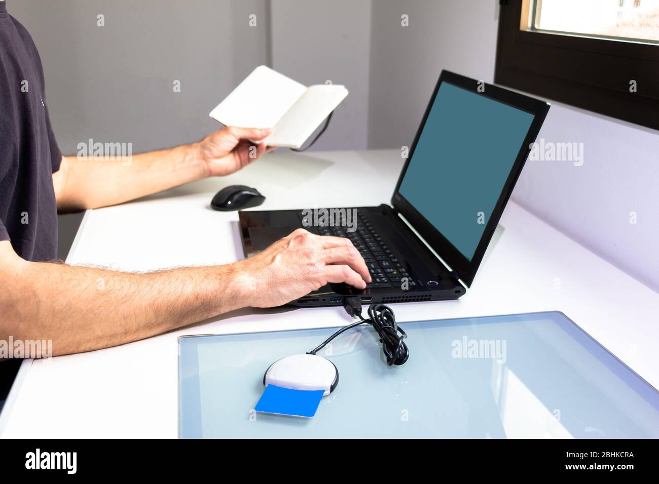 Close-up of the hands of a man working at home with his laptop, a notebook and identified by a card reader. Covid-19 confinement concept Stock Photo