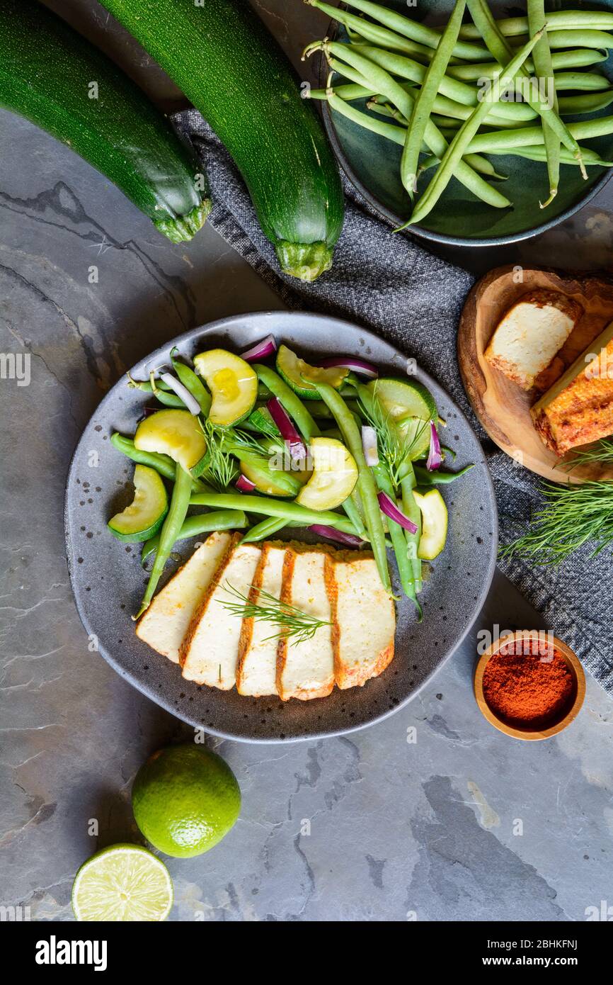 Marinated tofu slices served with blanched green beans and zucchini, drizzled with olive oil and decorated with fresh dill on a ceramic plate Stock Photo