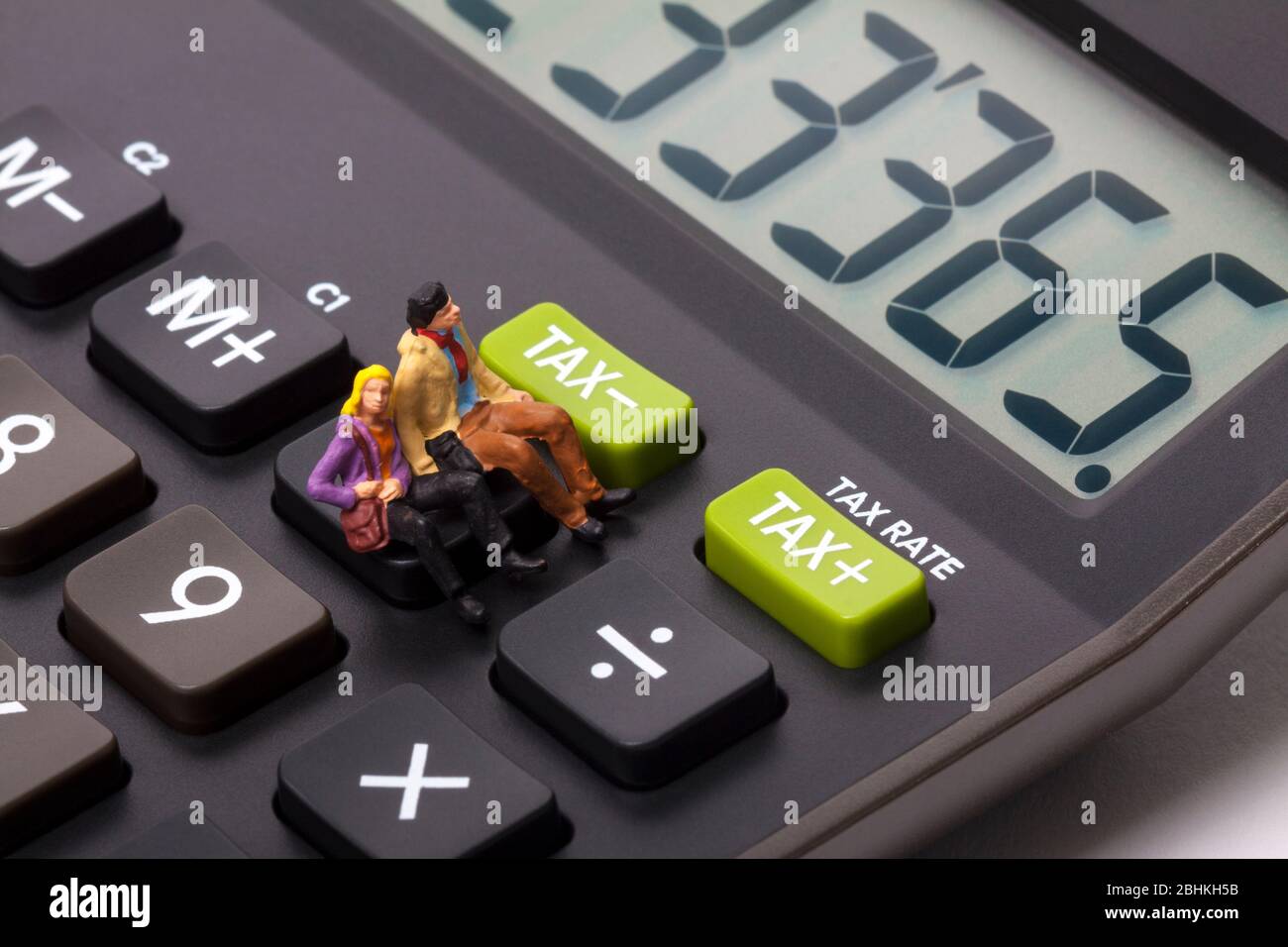 Conceptual image of miniature figure people sat on a calculator next to buttons marked tax Stock Photo