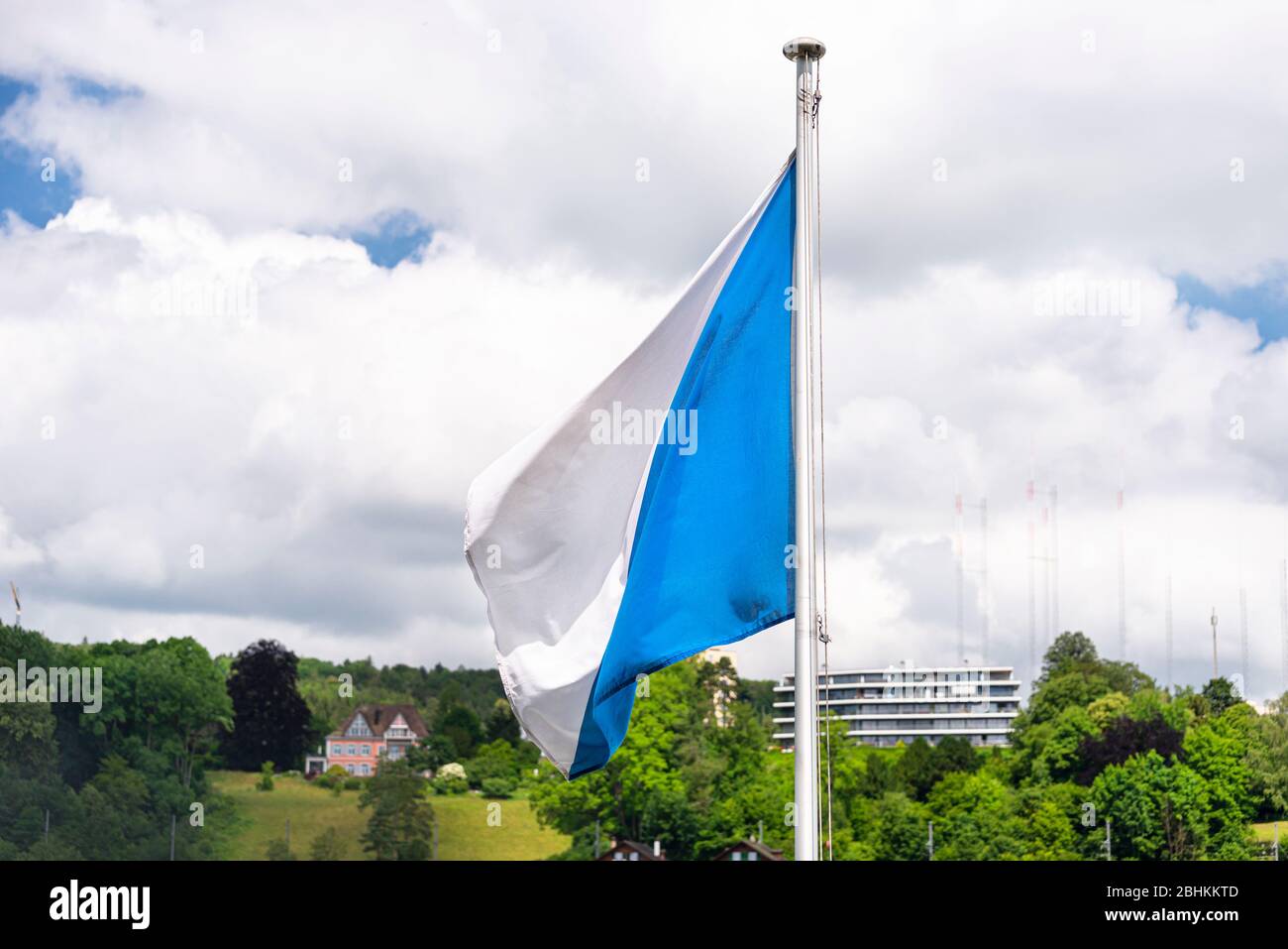 A white and blue flag hanging on the mast slightly fluttering to the left, white clouds in the background. Stock Photo