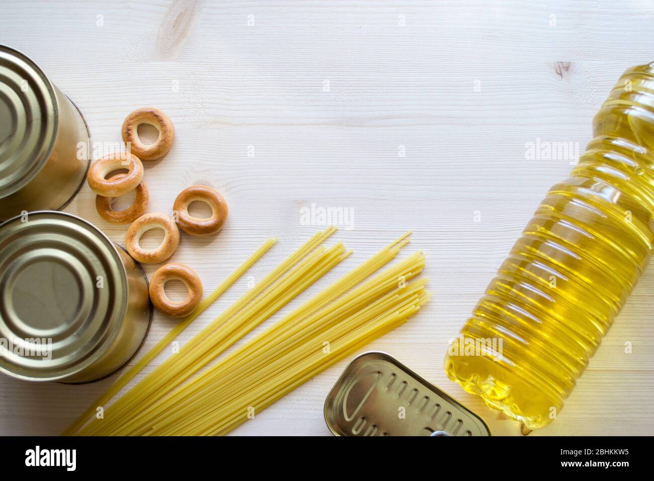 Food supplies, crisis food stock for quarantine isolation period on a bright wooden background. Pasta, oil, canned food, bagels. Stock Photo