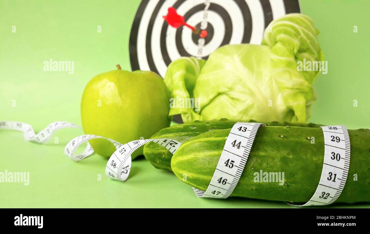 Fresh green vegetables and fruits wrapped in a measuring tape on a dart background.Concept of the goal to lose weight,the goal of diet. Stock Photo