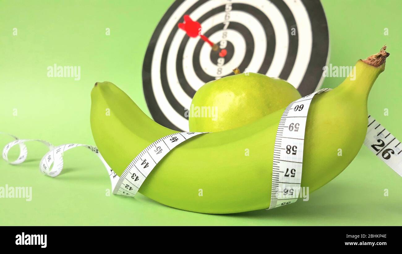 Fresh green fruits wrapped in a measuring tape on a dart background.Concept of the goal to lose weight,the goal of diet. Stock Photo