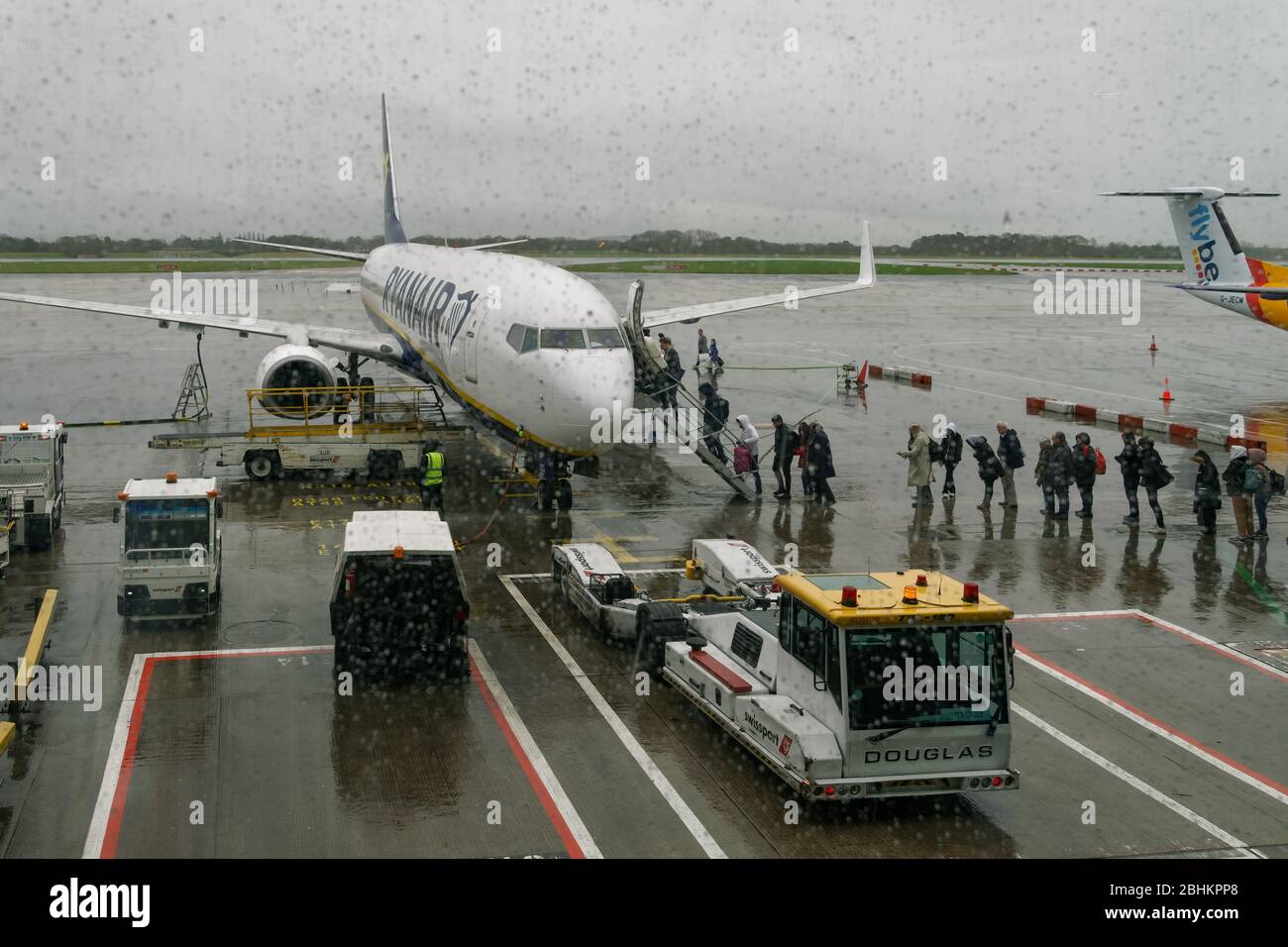 Manchester UK Ryanair aircraft with boarding passengers at airport tarmac. Rainy weather view of travelers at apron area entering a Boeing 737-800. Stock Photo