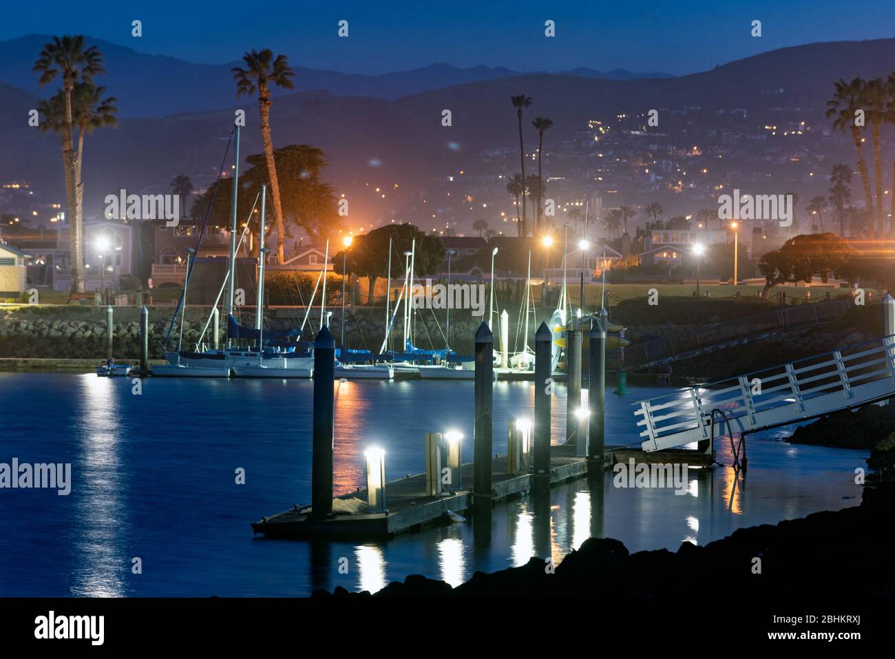 Emtpy cove dock illuminated by lamps on each pier as dawn breaks over the California coast. Stock Photo