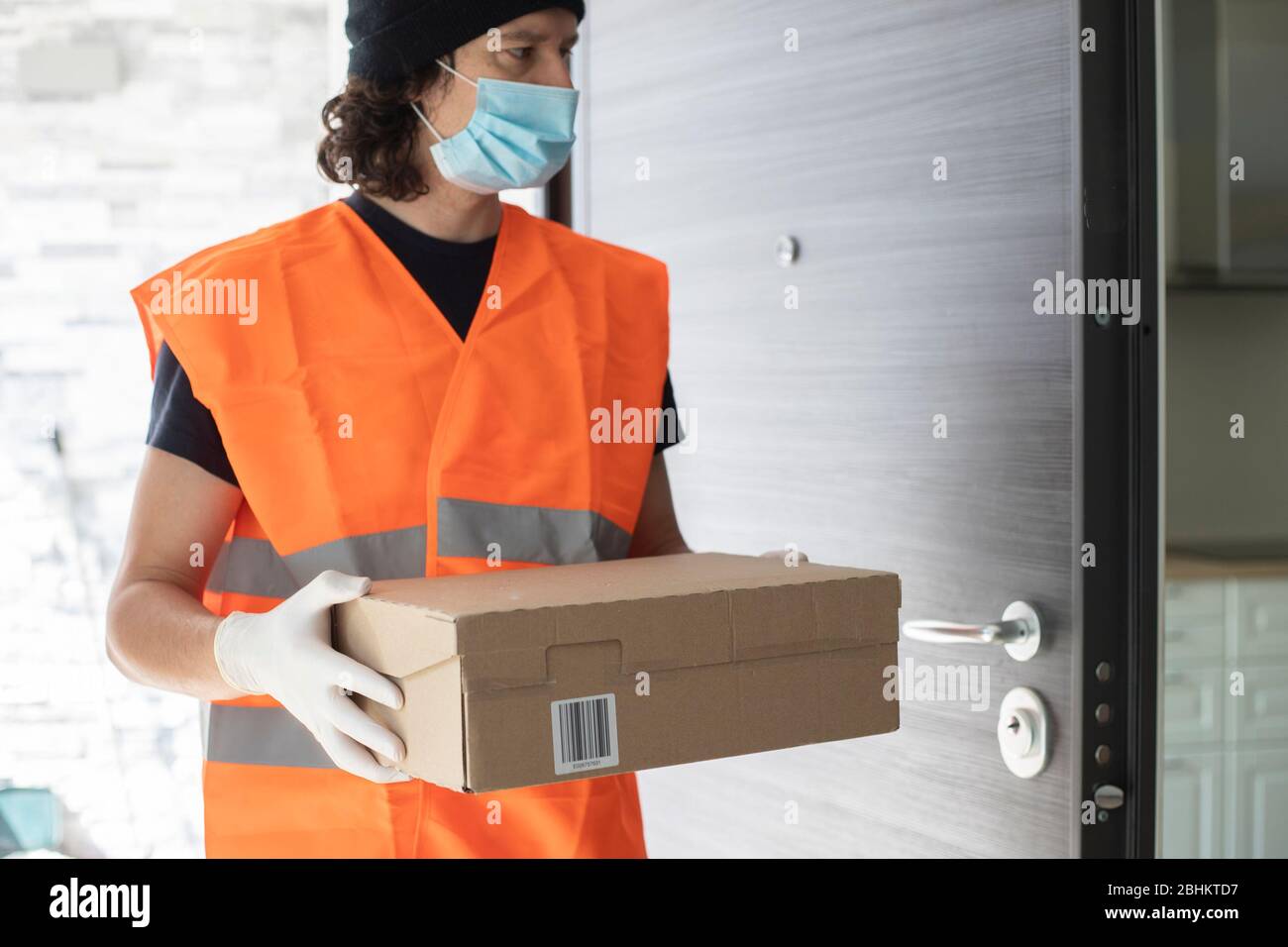 Young delivery man at front door with a parcel box, wearing gloves and