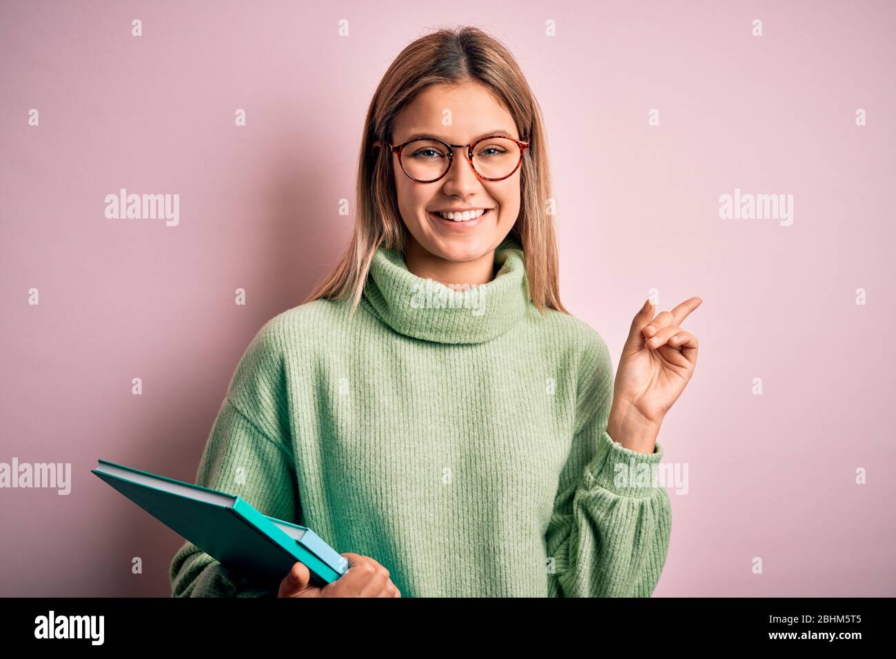 Young beautiful woman wearing glasses holding books over isolated pink  background very happy pointing with hand and finger to the side Stock Photo  - Alamy
