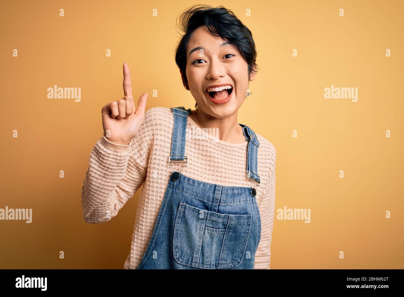 Young beautiful asian girl wearing casual denim overalls over isolated ...