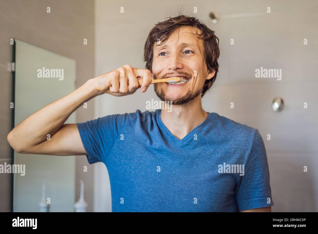 Personal hygiene concept. Pleased Caucasian young man carries bamboo toothbrush, satisfied to lead healthy lifestyle. Morning routine. Zero waste Stock Photo