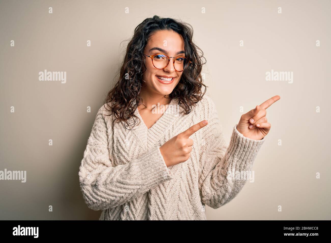 Beautiful woman with curly hair wearing casual sweater and glasses over ...