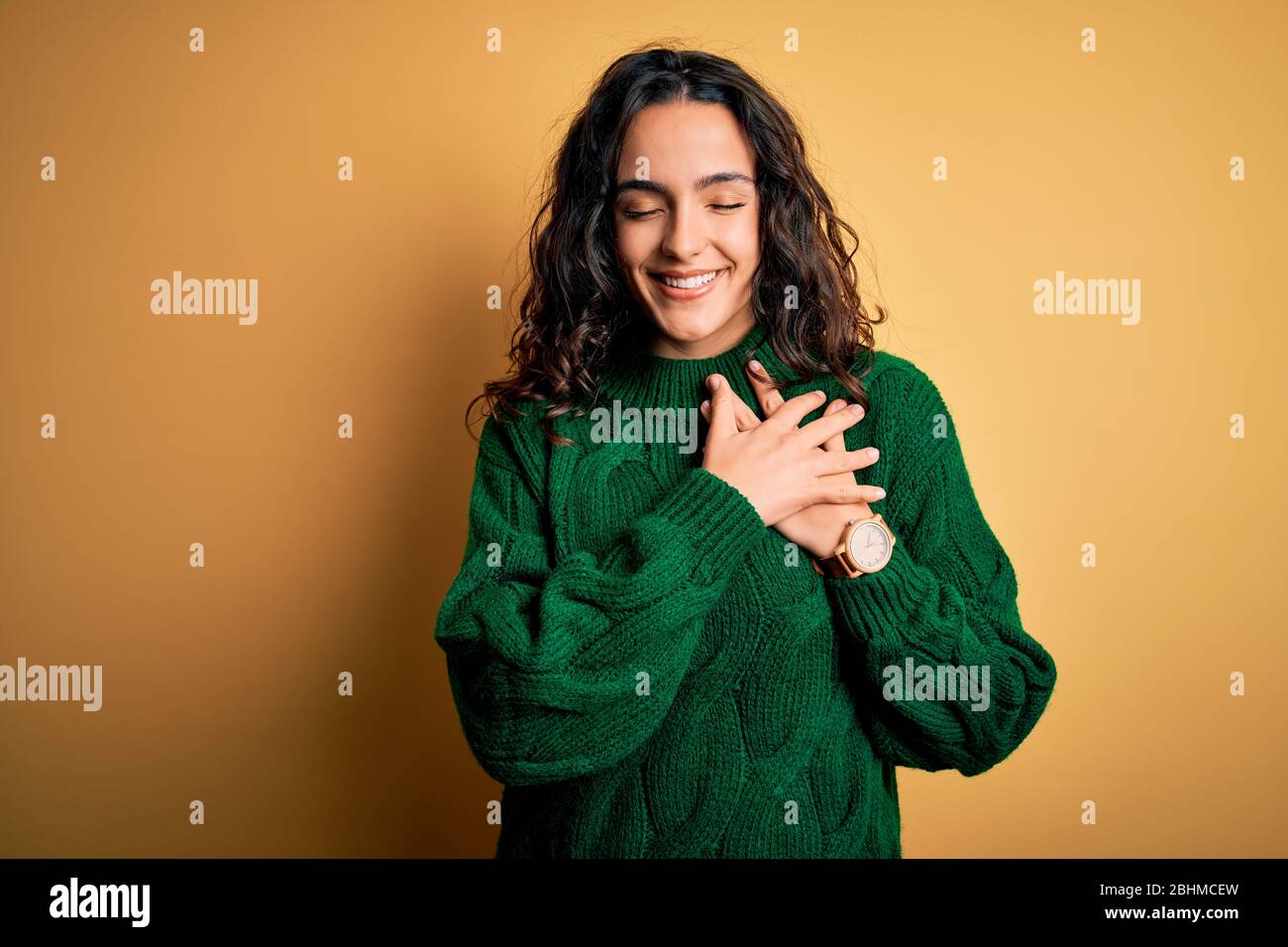 Young beautiful woman with curly hair wearing green casual sweater over ...