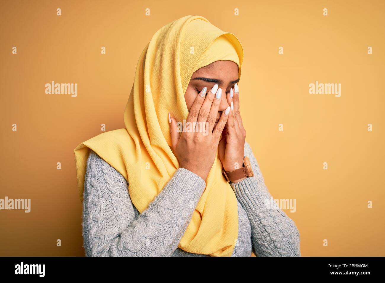 Young beautiful african american girl wearing muslim hijab over isolated yellow background rubbing eyes for fatigue and headache, sleepy and tired exp Stock Photo