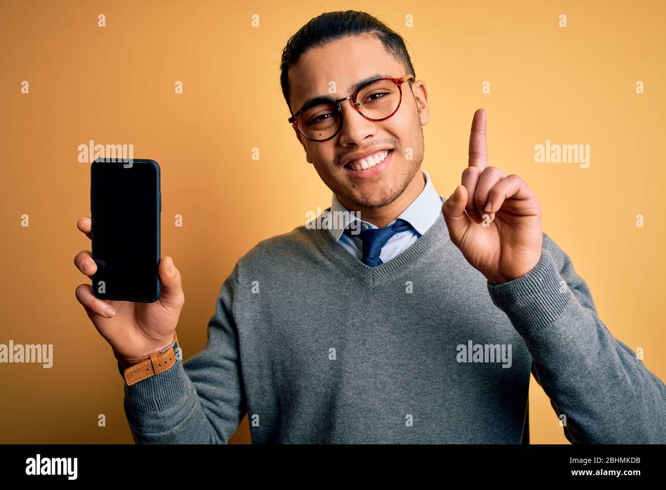 Young brazilian businessman wearing glasses holding smartphone showing