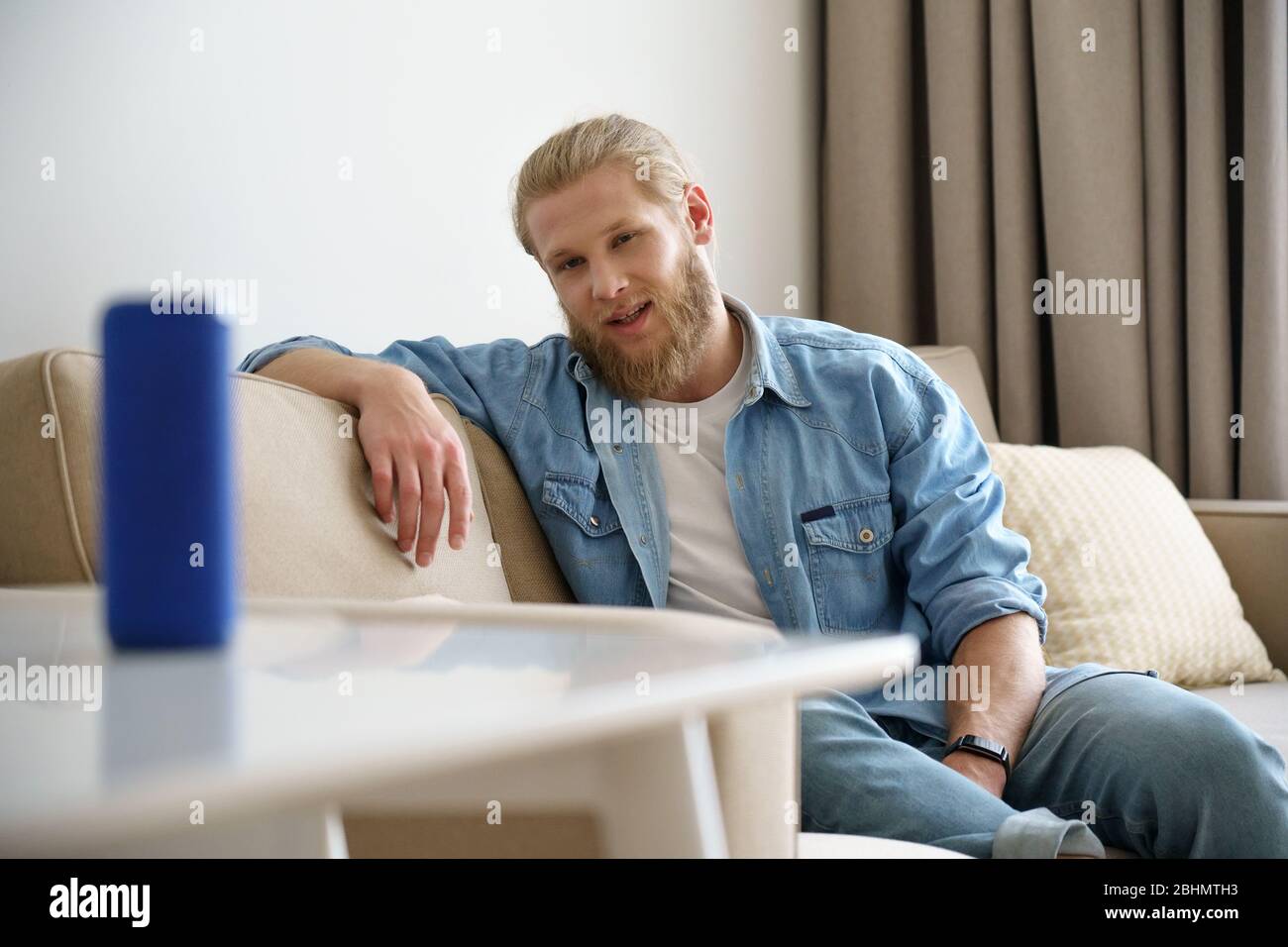 Young man speaking activating portable wireless speaker on table at smart home. Stock Photo