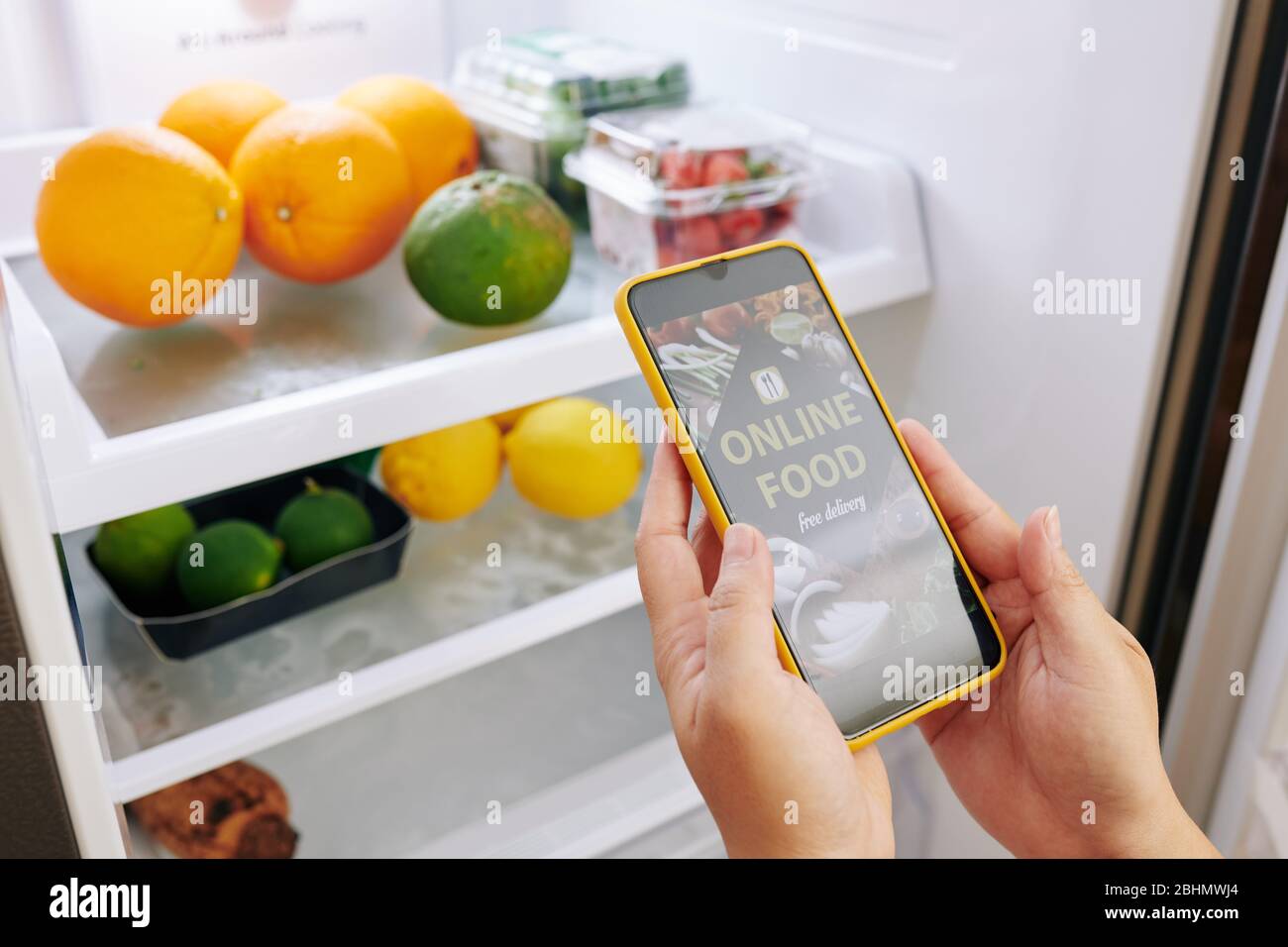 Close-up image of housewife opening refrigerator when observing what she has and ordering products via food delivery application on smartphone Stock Photo