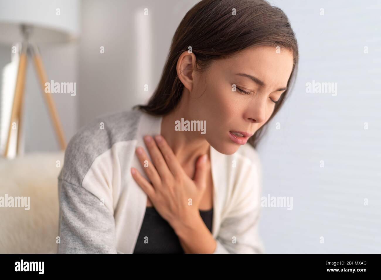 COVID-19 breathing difficulties woman with shortness of breath Coronavirus cough breathing problem. Asian girl in pain touching chest respiratory symptoms fever, coughing, body aches. Stock Photo