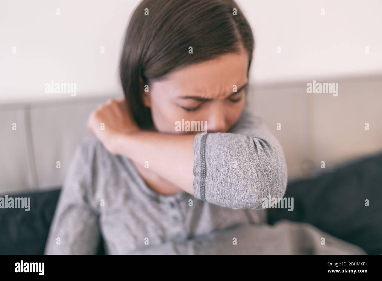 COVID-19 cover cough Coronavirus reducing of risk of spreading the infection by covering nose and mouth when coughing and sneezing with flexed elbow. Young girl at home cough in arm prevention. Stock Photo