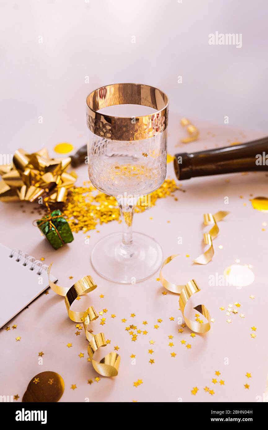 glass with a gold border with yellow circles and gold spirals serpentines, dark glass bottle and a wine opener in the background. Stock Photo