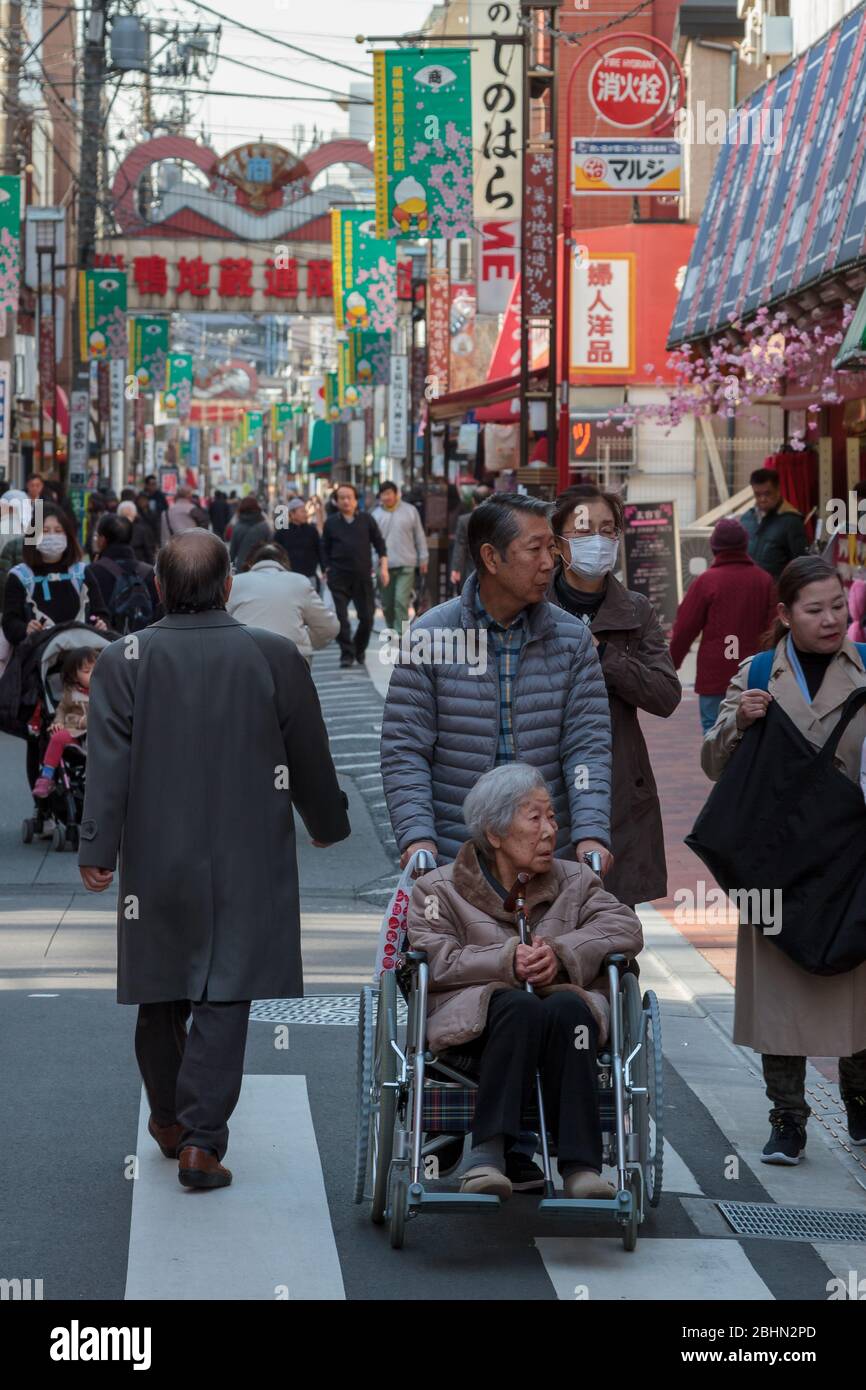 A man pushes an older Japanese woman, in a wheelchair down the main Jizo Dori street in Sugamo, Tokyo, Japan. Stock Photo
