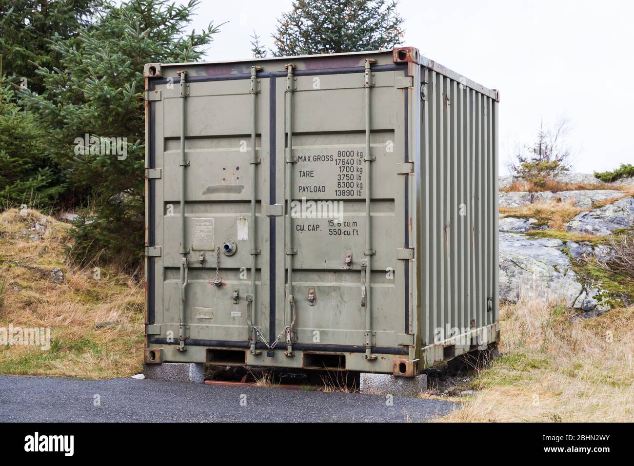 Military green cargo container stands on grass, industrial shipping equipment Stock Photo