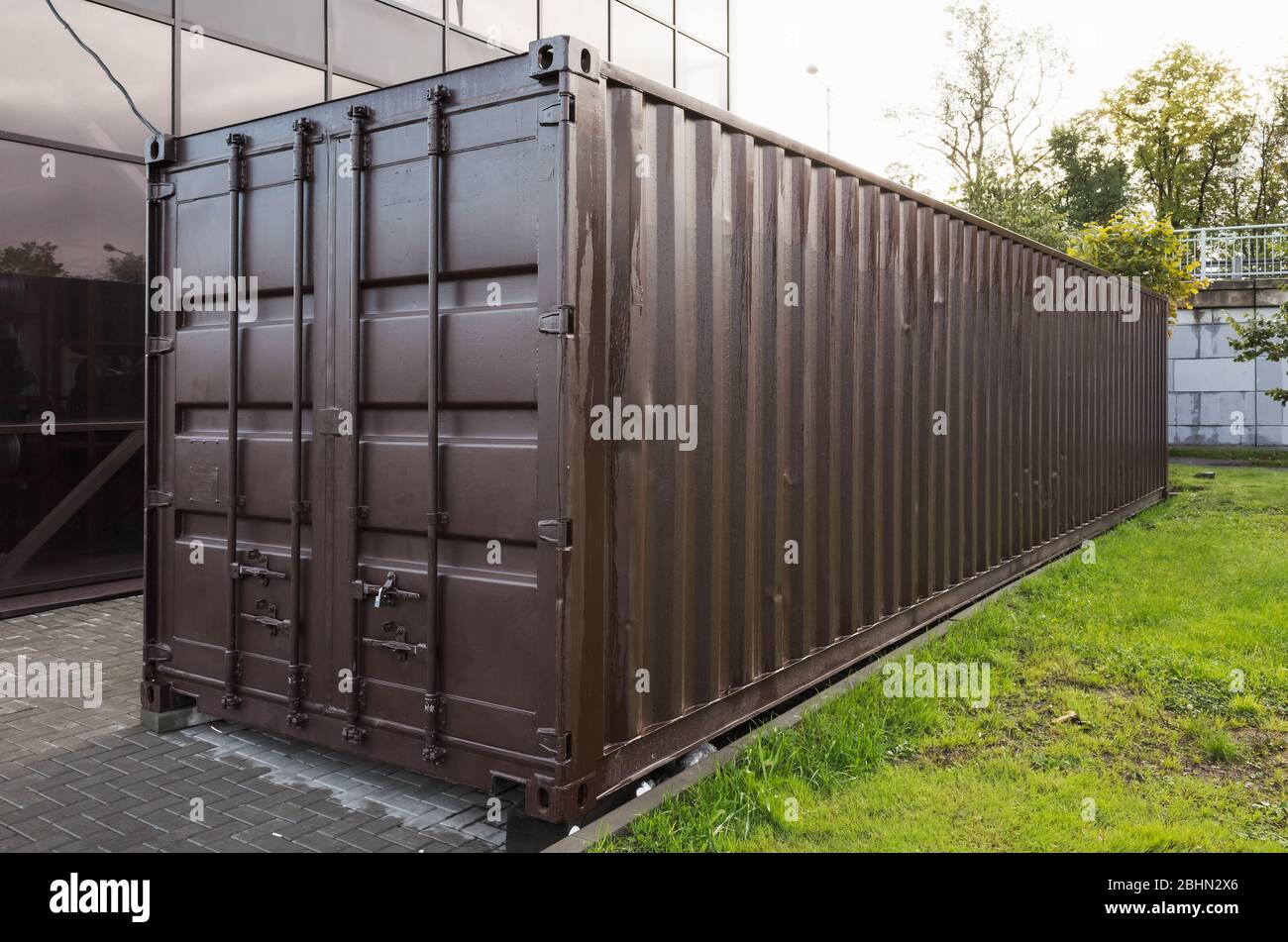 Dark brown cargo container stands near green grass, modern industrial shipping equipment Stock Photo